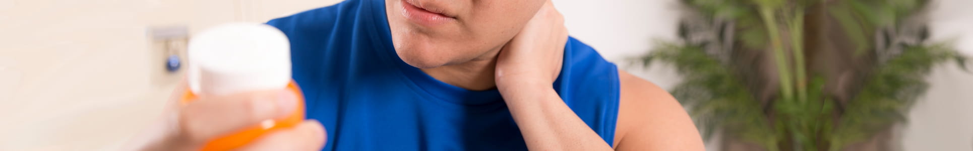 Man massaging neck in pain and holding and looking at medicine bottle