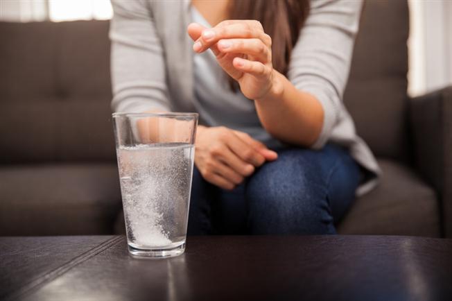 Woman dropping antacid into glass Woman dropping antacid into glass