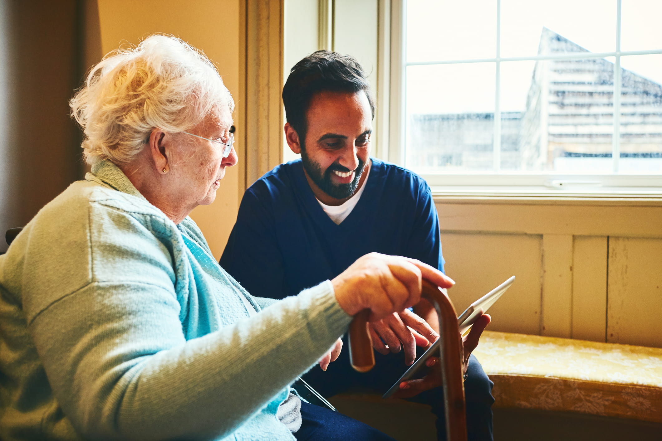 Younger person working with an older lady to show her how to use a tablet