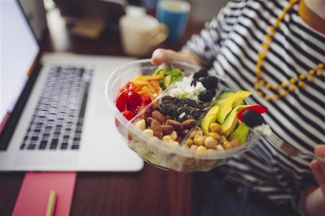 Close-up of person holding up a salad bowl while sitting at desk in front of laptop Close-up of person holding up a salad bowl while sitting at desk in front of laptop