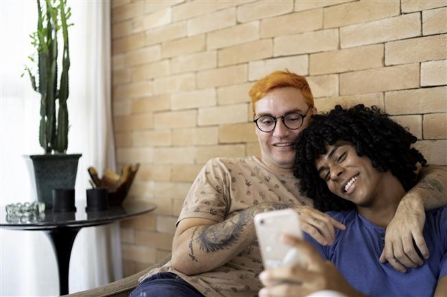 Young gay couple on couch at home looking at cell phone
