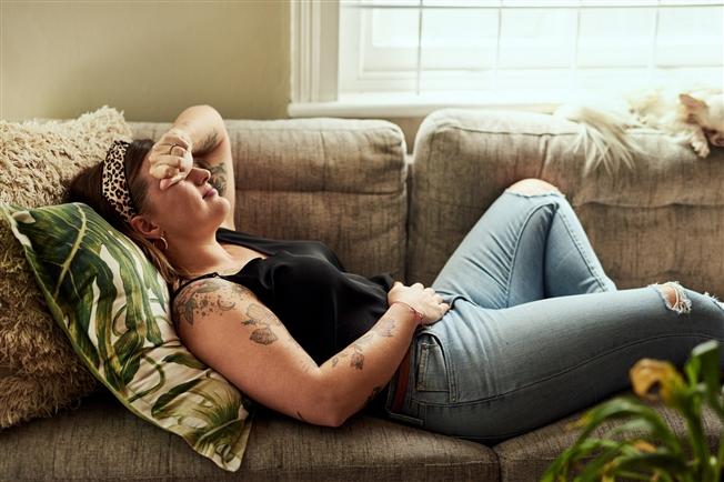 Young woman laying on couch grimacing in pain with hand to stomach