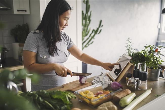 Middle aged woman cooking in kitchen reading recipe on ipad