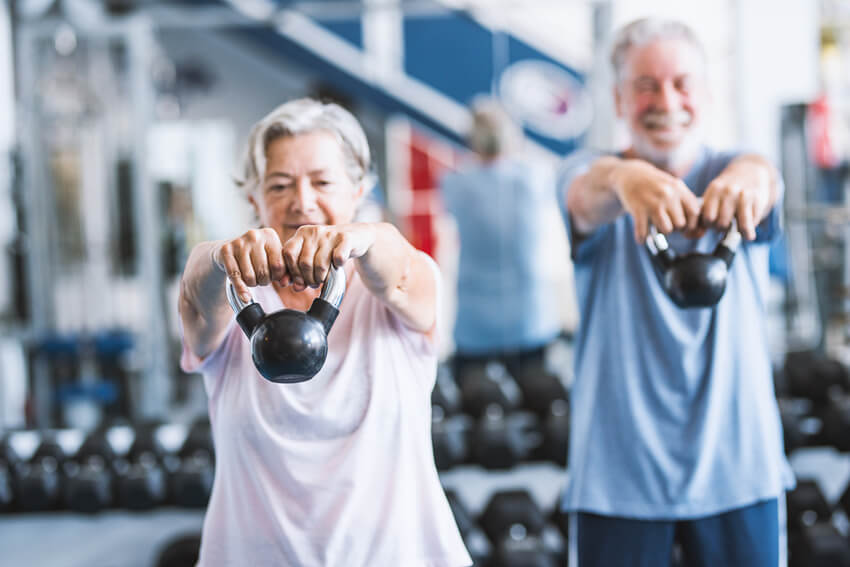 A senior male and female doing strength exercise in the gym together.