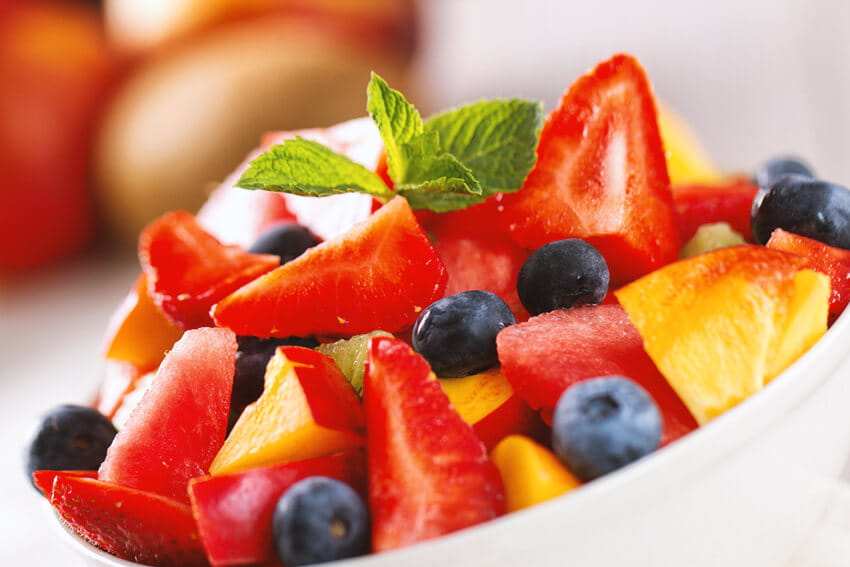 Strawberry, blueberry and peach fruit salad with mint.