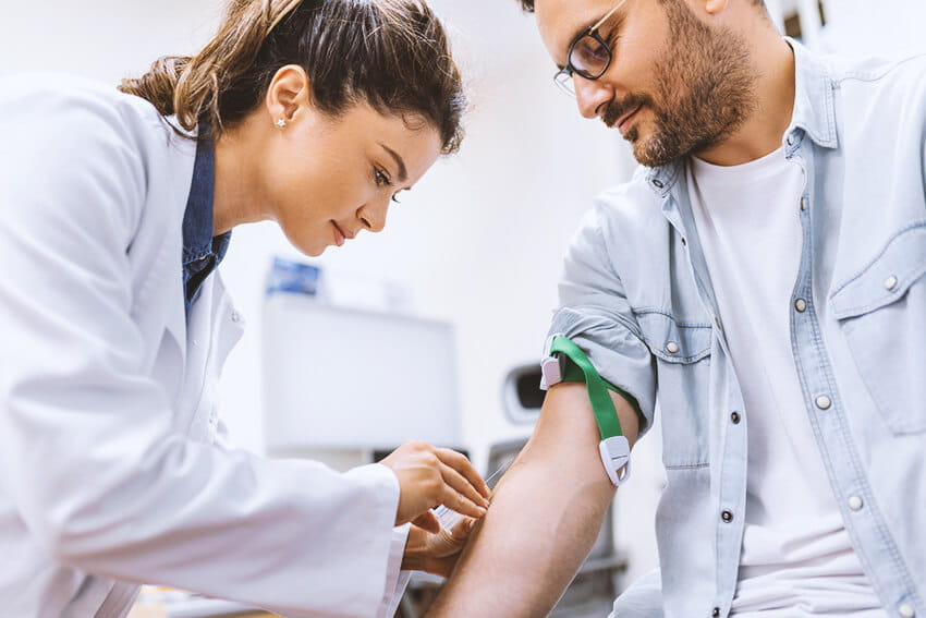 Hospital phlebotomist collecting blood sample from patient in lab.