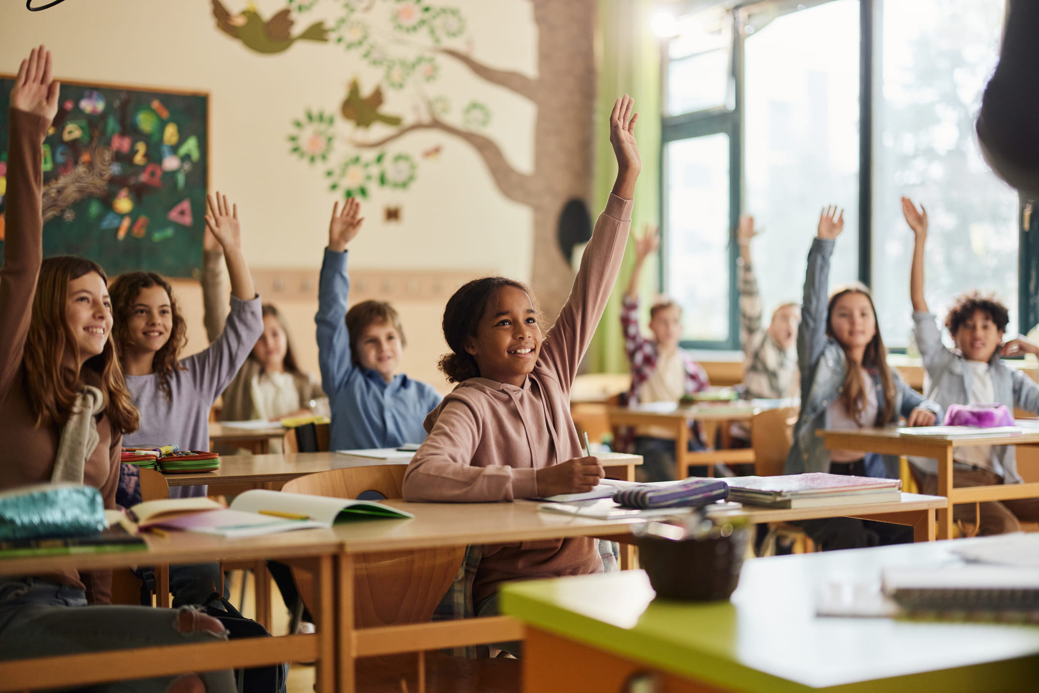 Happy elementary students raising their hands on a class at school