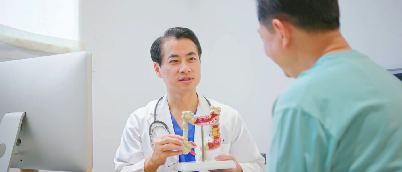 Asian male doctor showing large intestine model to an older male patient