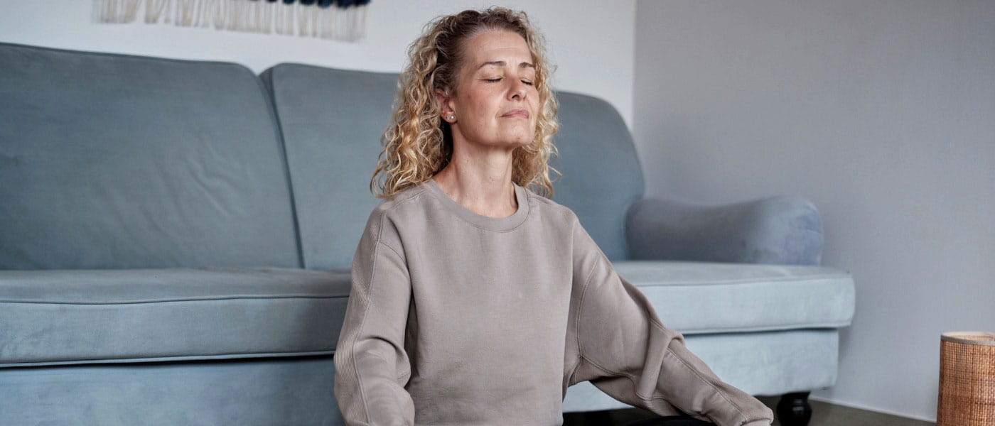 Middle-aged woman sitting in lotus pose on living room floor