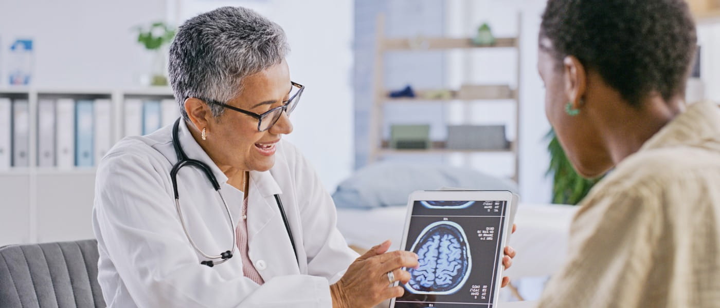 older female medical professional pointing at a brain scan on a tablet device and explaining to a female patient