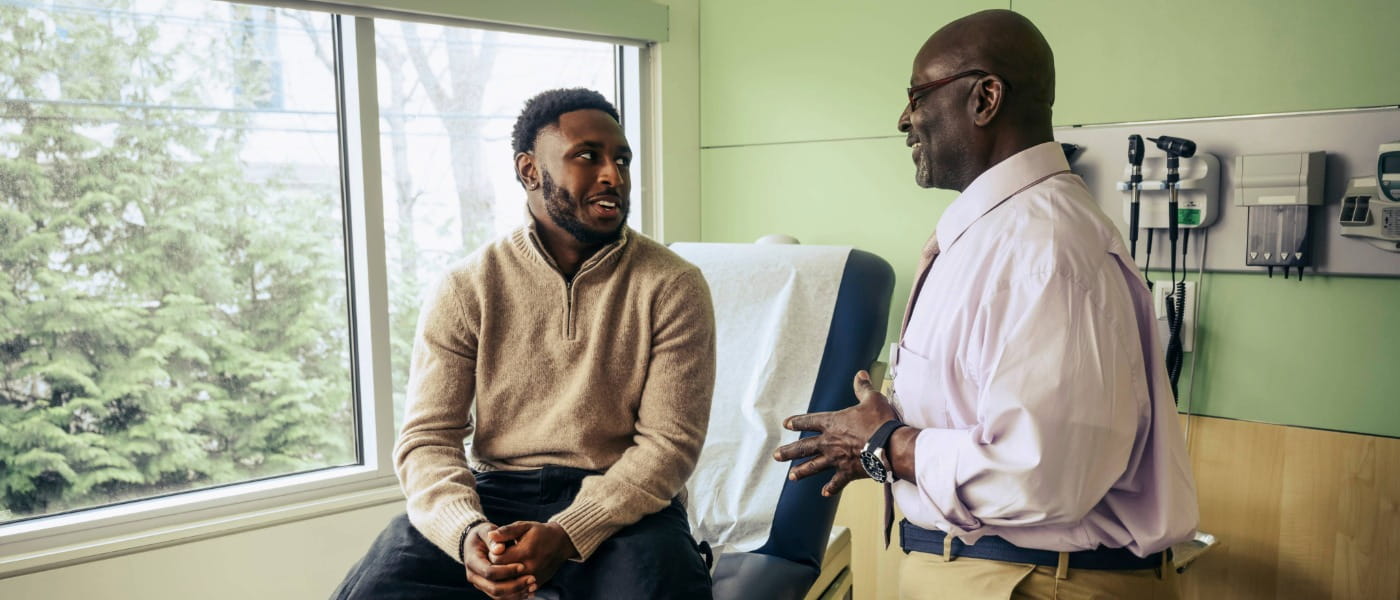 an older African American male doctor advising an adult African American man on his exam table