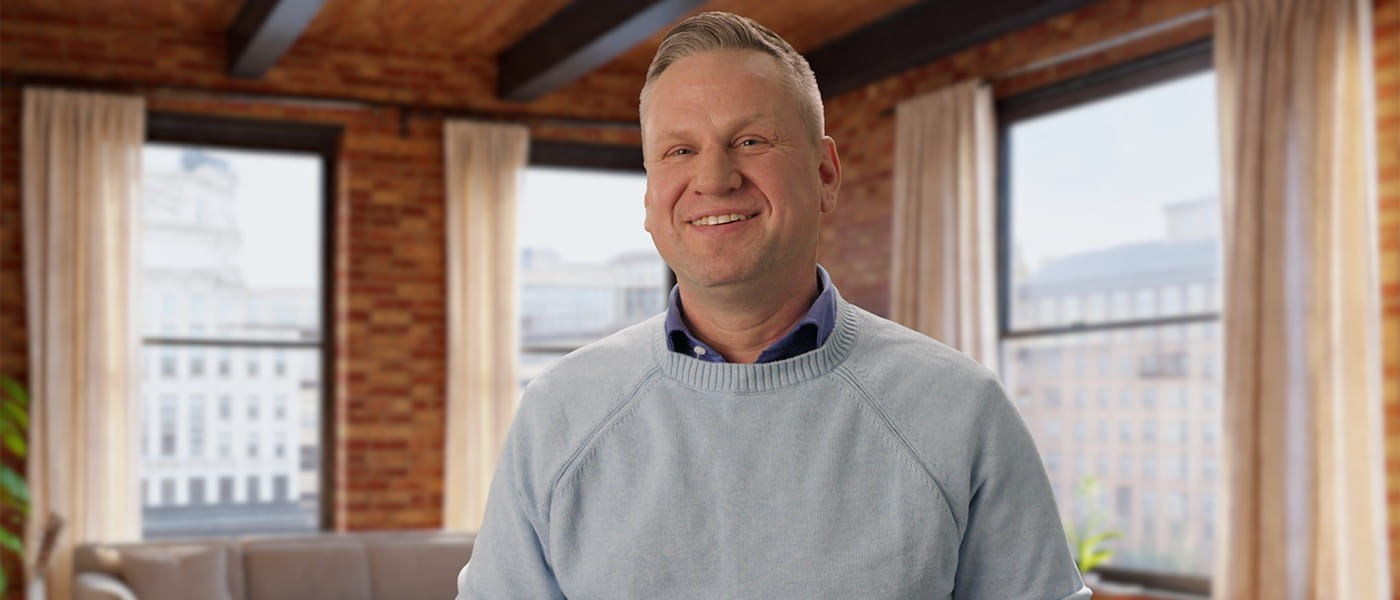 Kevin Hart smiling with a living room and windows behind him.