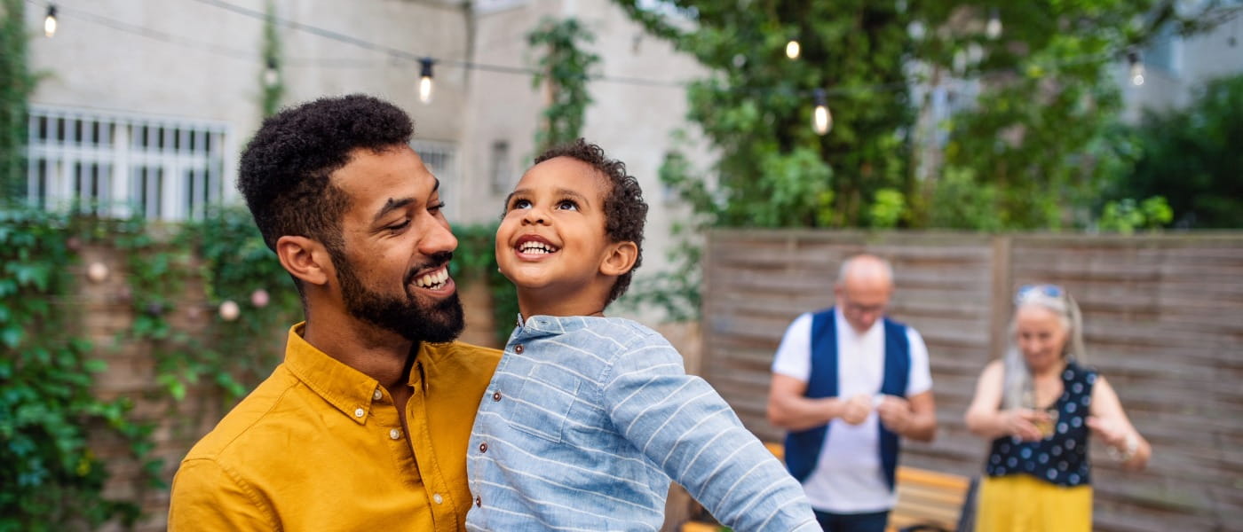 Happy young father holding his little son laughing and having fun during family dinner outdoors in back yard.