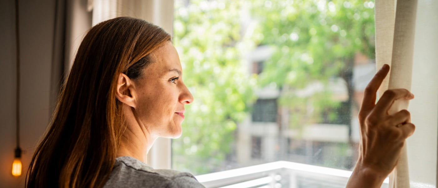 Mid adult woman smiling while looking through a window open to blossoming trees.