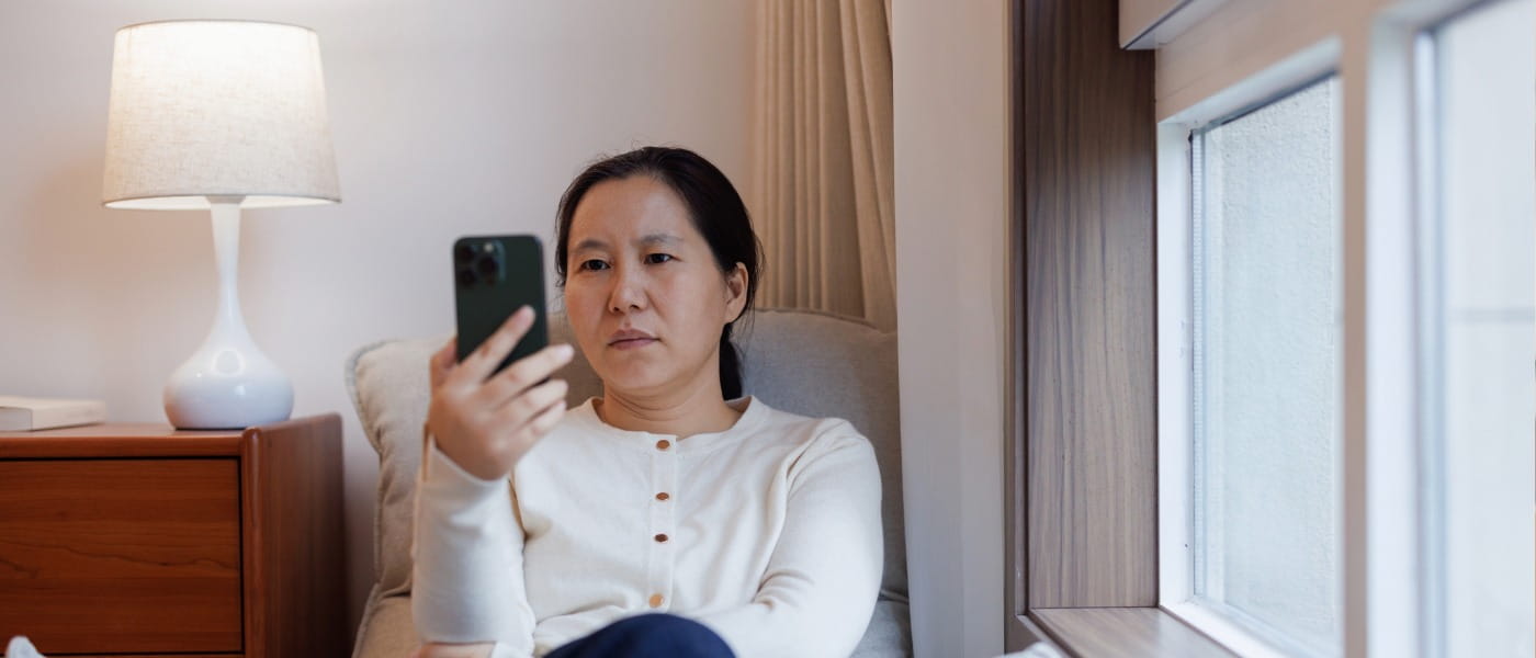 A middle-aged woman looking at her mobile phone with a look of concern on her face.