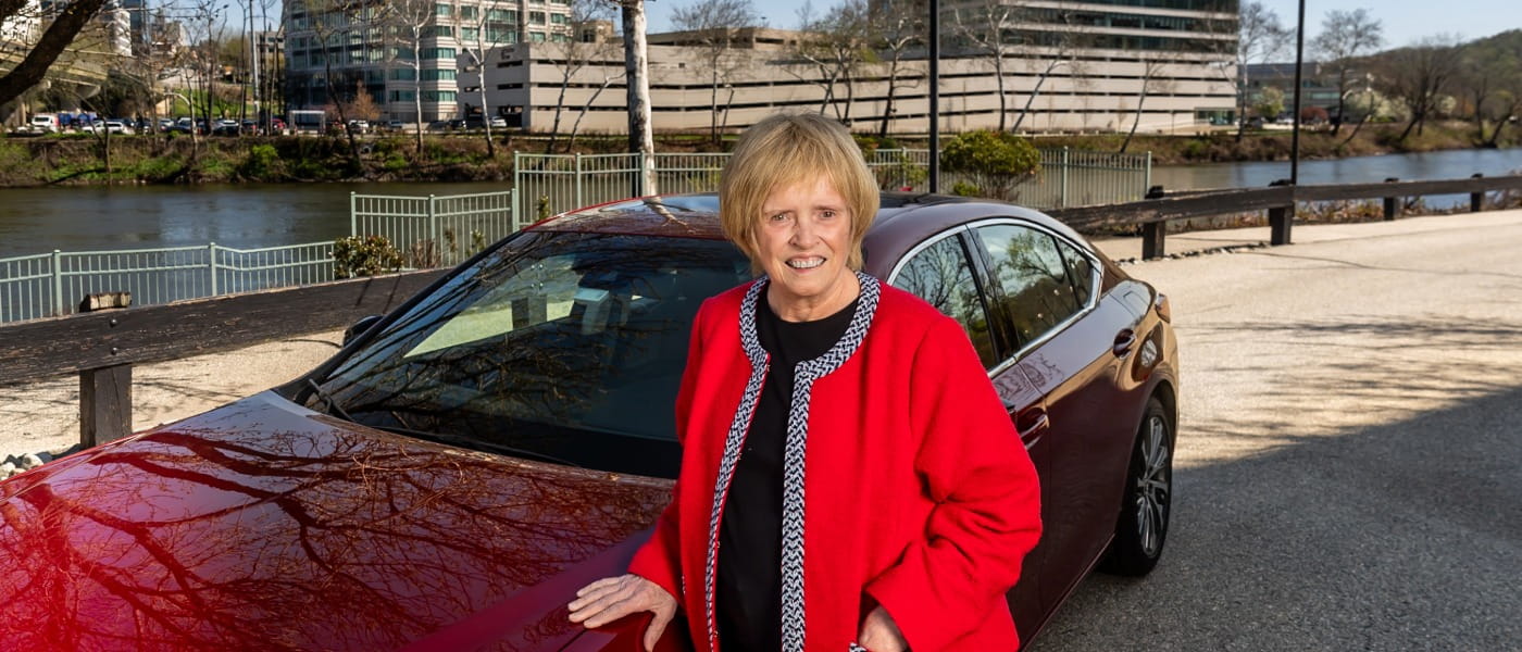 Celeste Nasuti in front of her red car next to a river in a city.