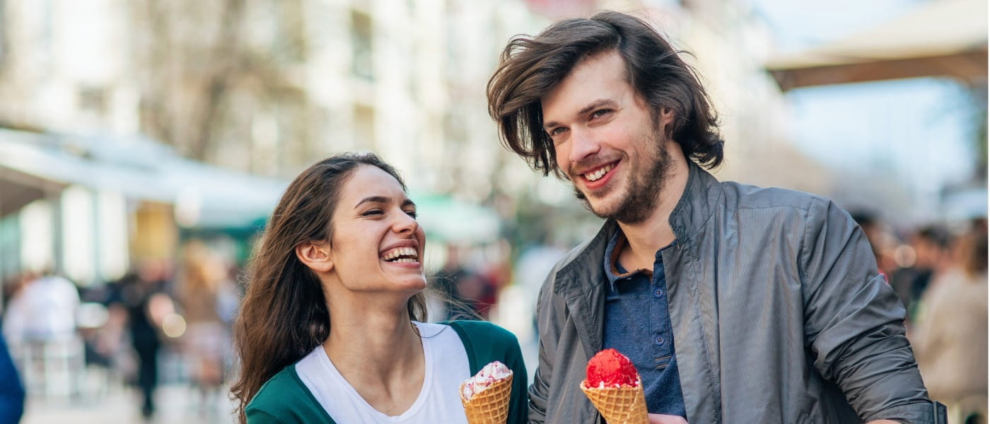 Young adult woman and man walking outdoor in the city with ice cream, smiling, looking happy and in love.