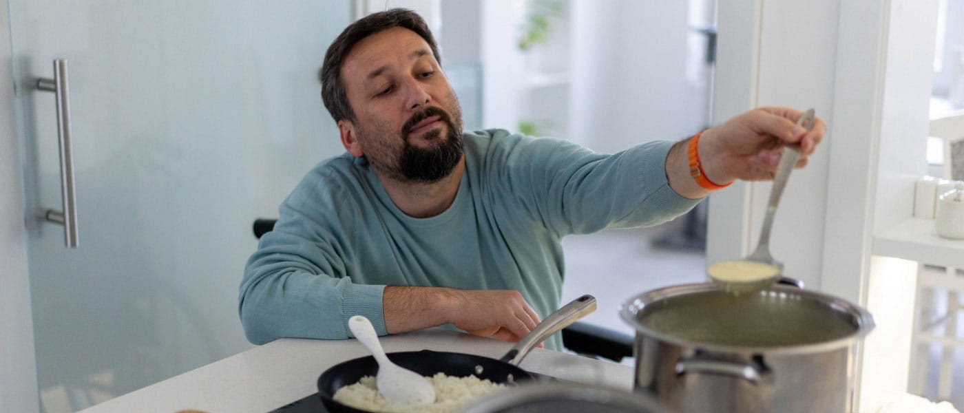 A man in a wheelchair prepares a meal in a bright and accessible kitchen, demonstrating independence and adaptability after completing occupational therapy.