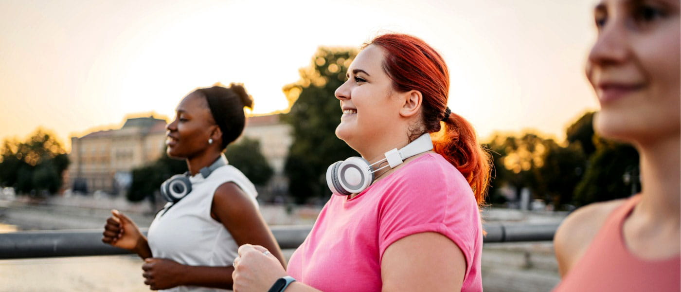 Three young female friends smiling while jogging on a bridge together at sunset.