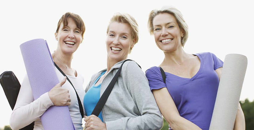 Three women getting ready for yoga holding their mats Three women getting ready for yoga holding their mats
