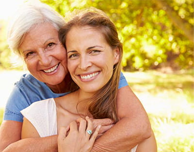 An older mother and daughter hugging and posing for the camera outside